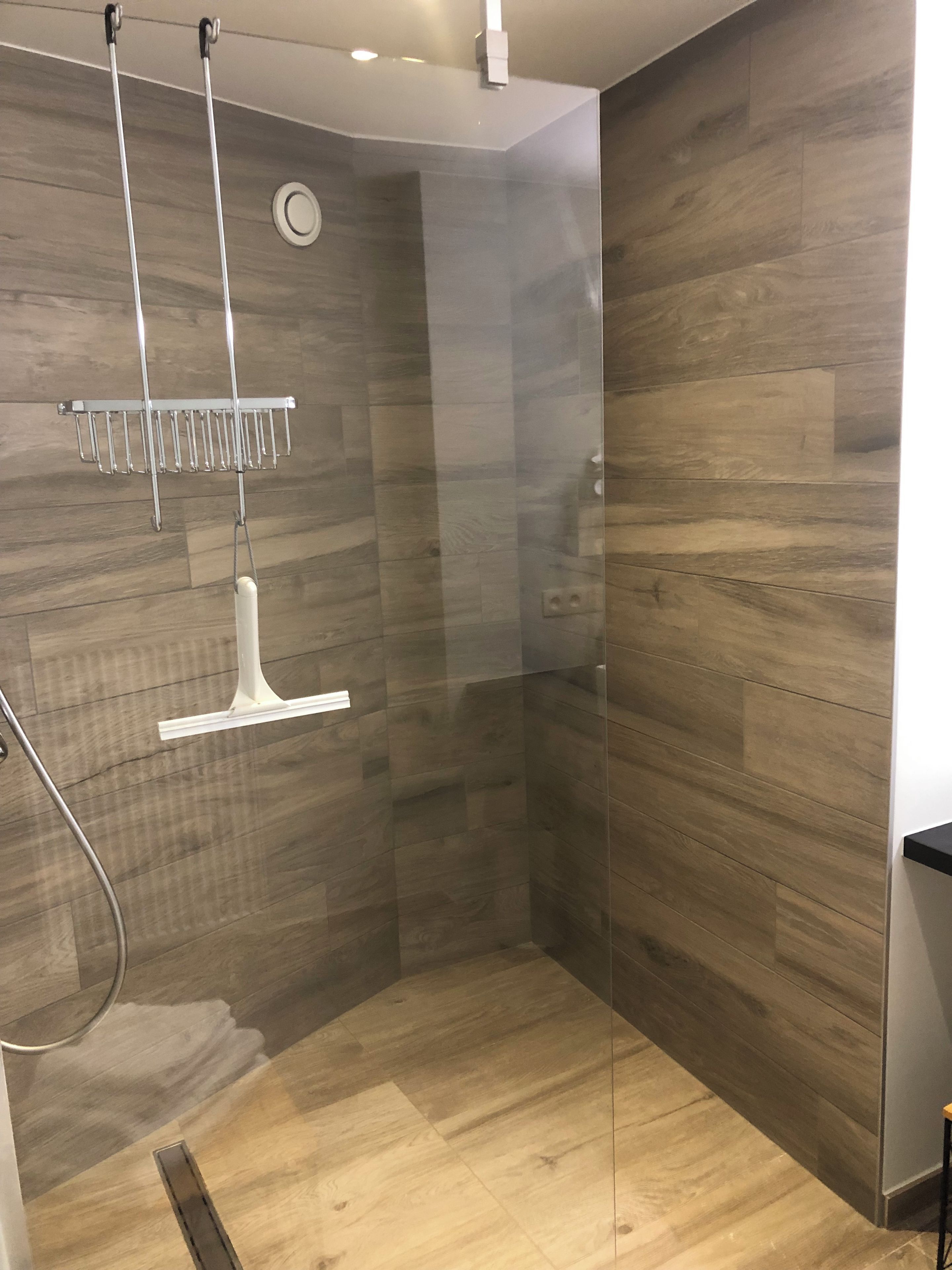 A modern shower with a glass door, a metal rack, and a white light fixture.