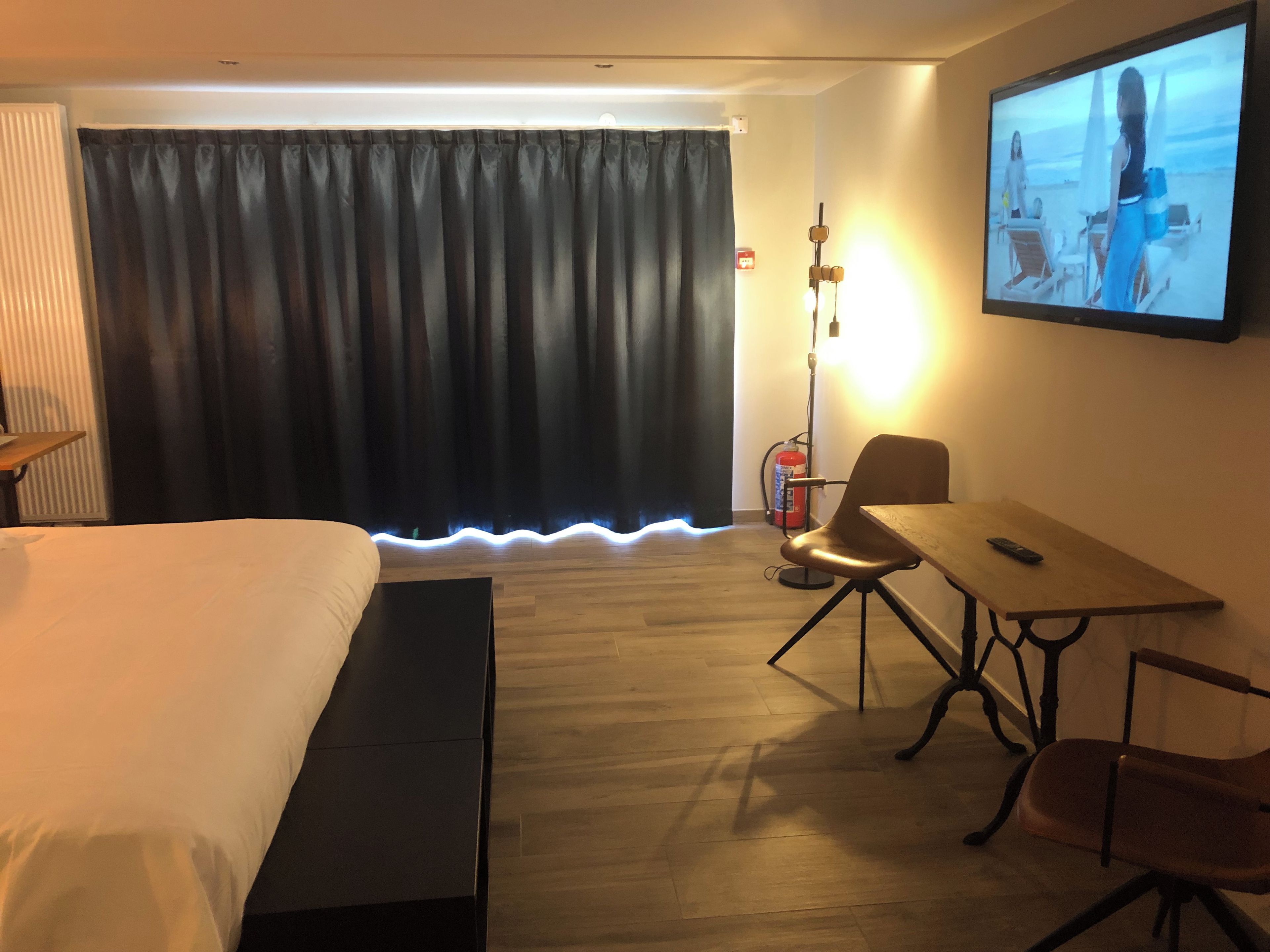 A hotel room with a bed, a desk, a chair, a television, and a curtain.