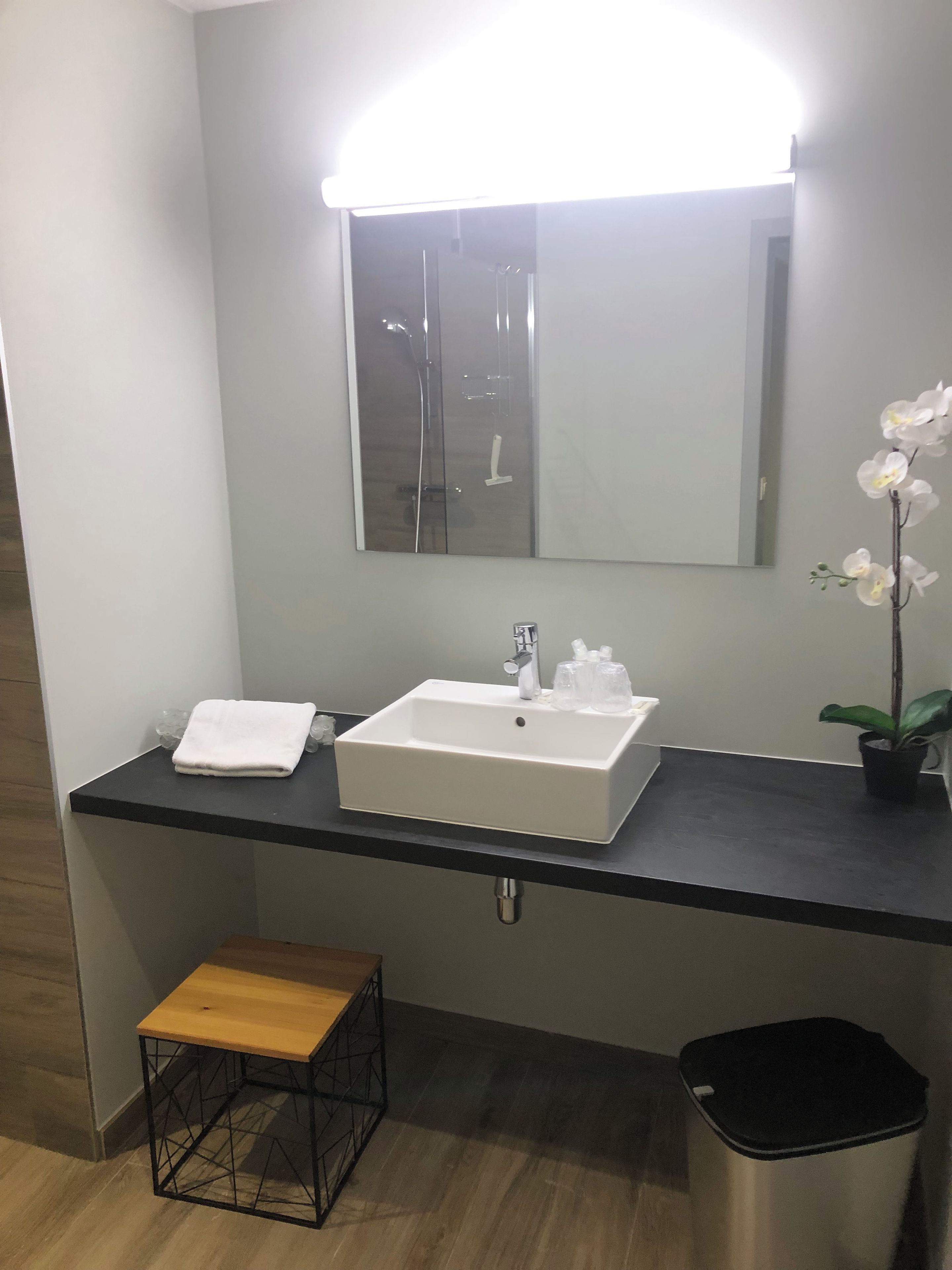 A bathroom with a white sink, a mirror, a towel, a small stool, and a trash bin.