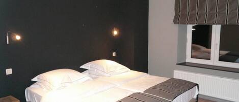 A bedroom with a bed, two bedside lamps, a window with curtains, and a radiator.