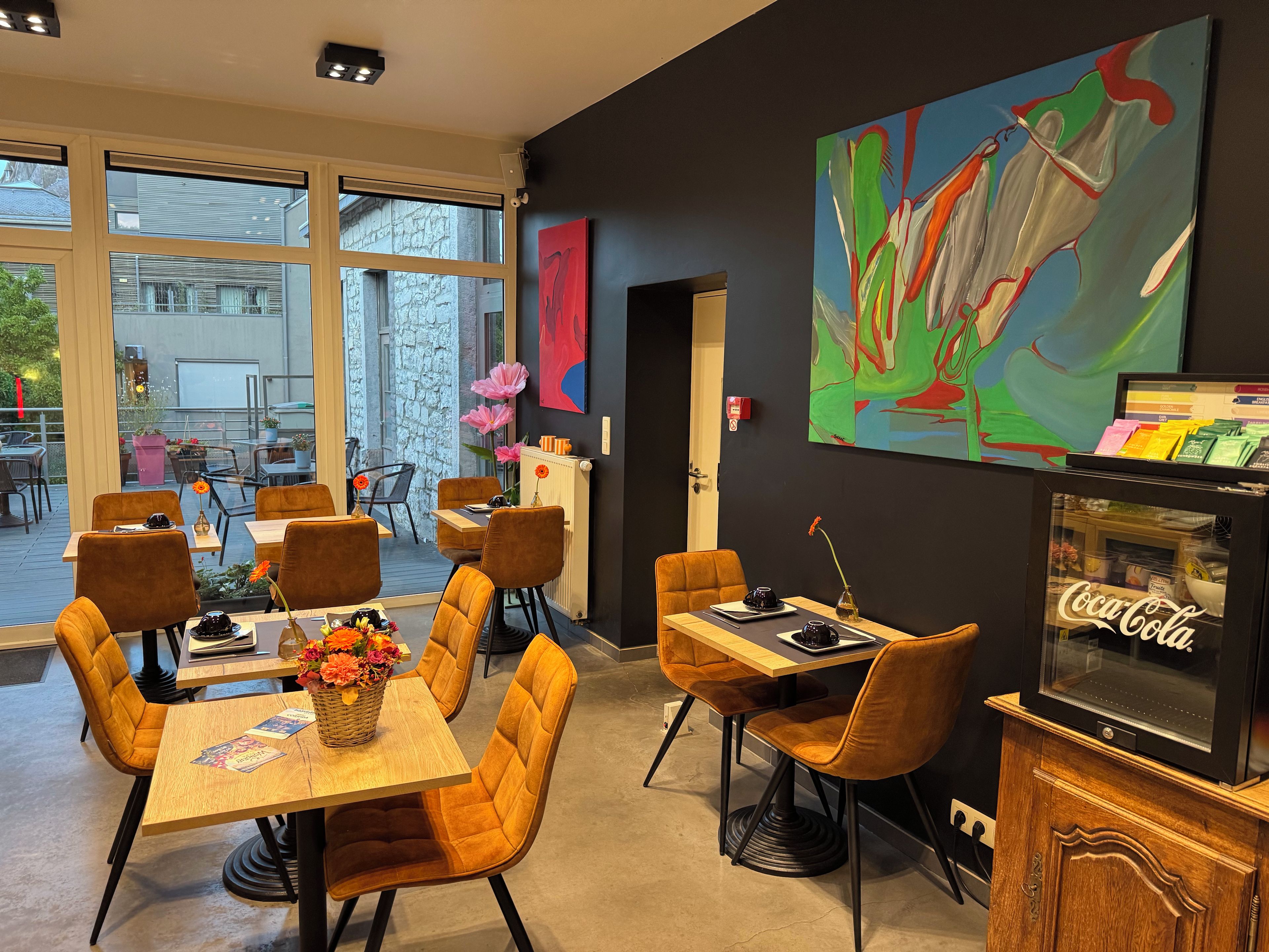 A modern dining area with tables and chairs, a large window, and a wall-mounted abstract painting.
