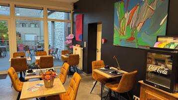 A modern dining area with tables and chairs, a large window, and a wall-mounted abstract painting.