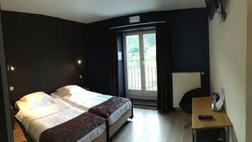 A bedroom with two beds, a window with curtains, a radiator, and a small table with a remote control.