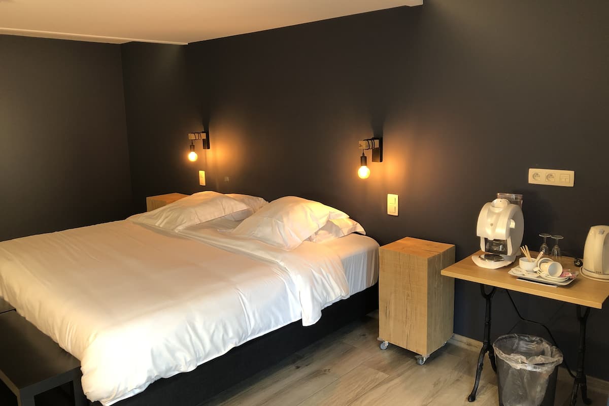 Una habitación de hotel moderna con una cama grande, mesitas de noche, una cafetera y un cubo de basura.