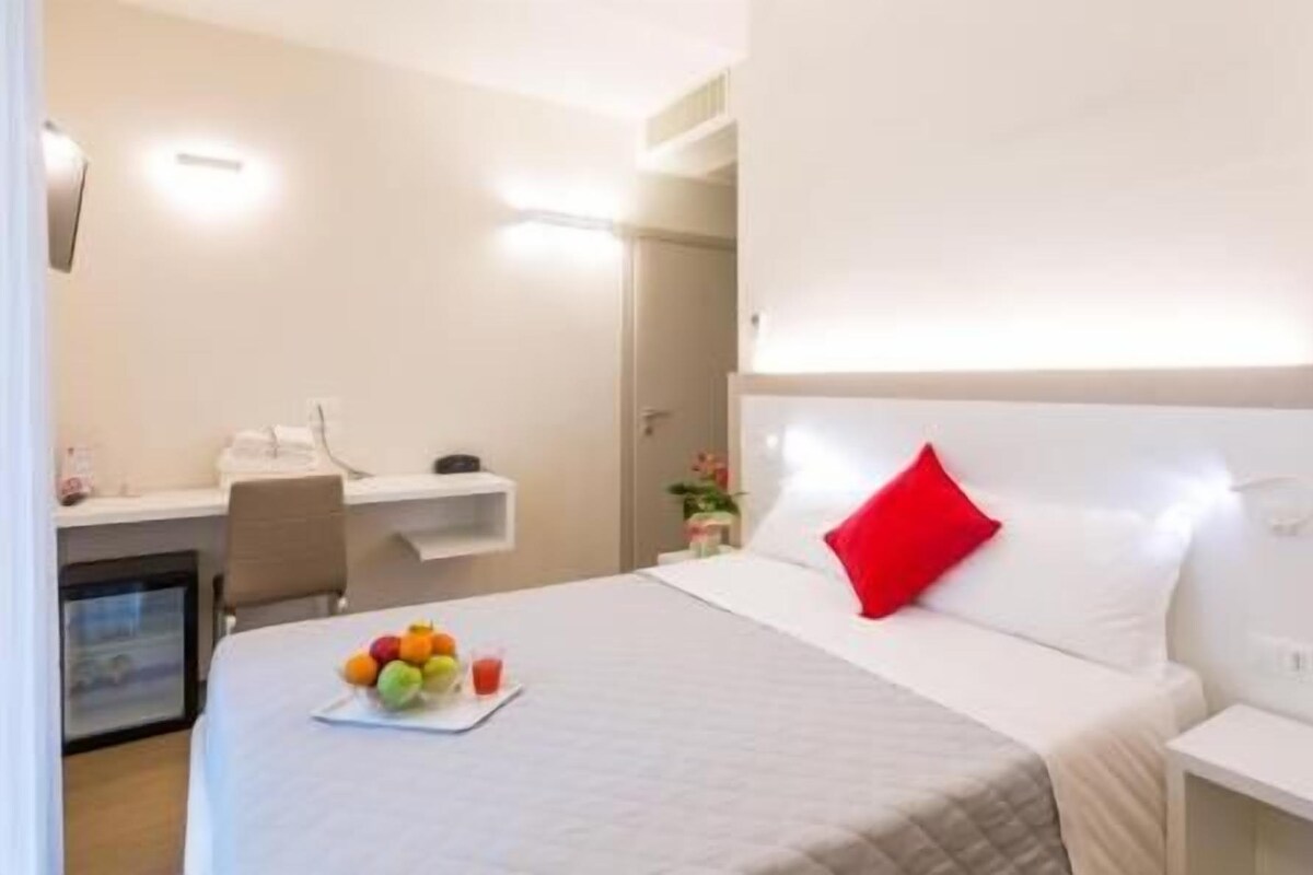 A hotel room with a bed, bedside table, and a desk with a chair.