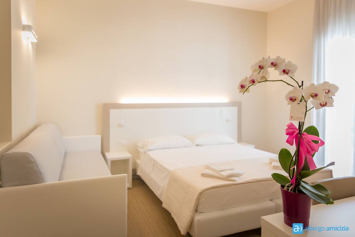 Quarto de hotel com cama, mesa de cabeceira, cadeira e uma orquídea em vaso.