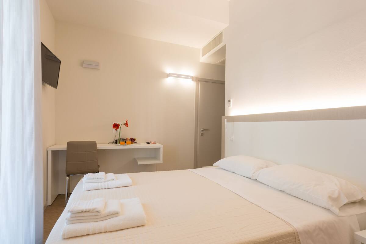 Quarto de hotel com cama, escrivaninha e cadeira.