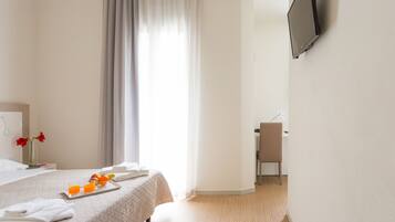 Ein Hotelzimmer mit Bett, Schreibtisch mit Stuhl, einem an der Wand befestigten Fernseher und einem Fenster mit Vorhängen.