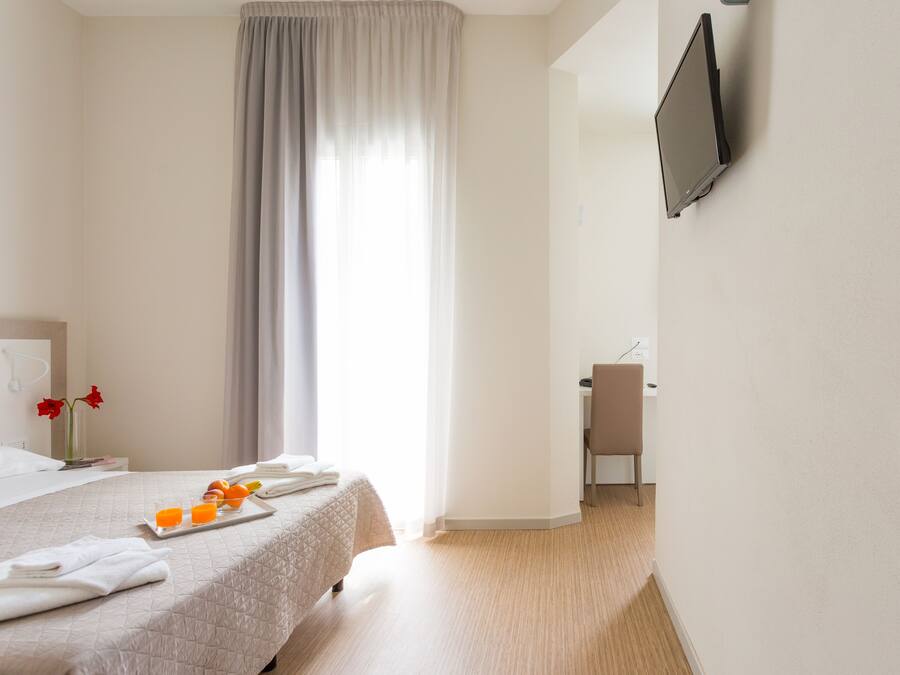 Ein Hotelzimmer mit Bett, Schreibtisch mit Stuhl, einem an der Wand befestigten Fernseher und einem Fenster mit Vorhängen.