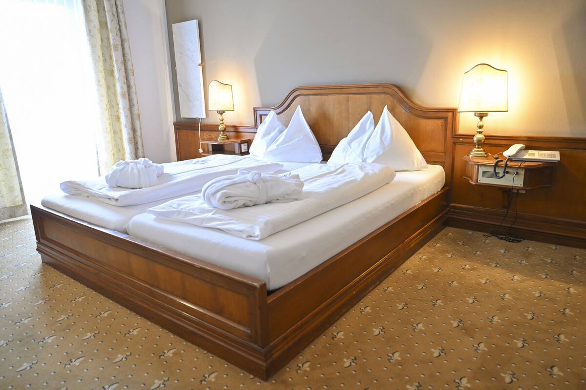 A neatly made bed with pillows and towels, a wooden headboard, bedside lamps, and a telephone on a nightstand.