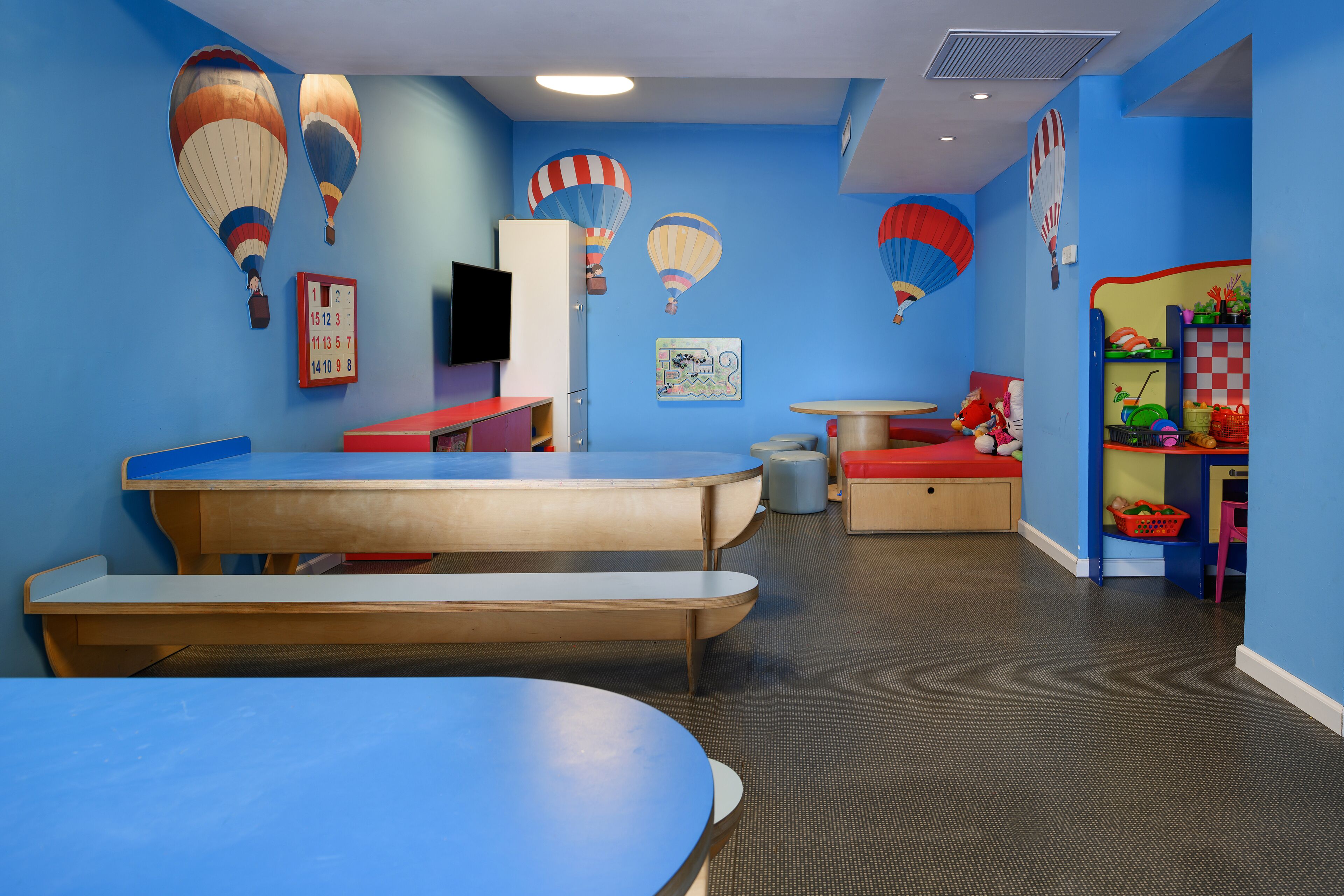 A children's playroom with tables, chairs, and hot air balloon decorations on the walls.