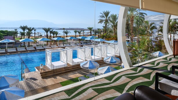 A poolside area with lounge chairs and umbrellas, a clear view of the sea, and a modern architectural design. - Noga By Isrotel Collection (Tamar)