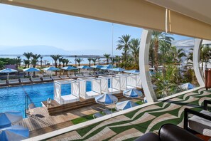 A poolside area with lounge chairs and umbrellas, a clear view of the sea, and a modern architectural design. - Noga By Isrotel Collection (Tamar)
