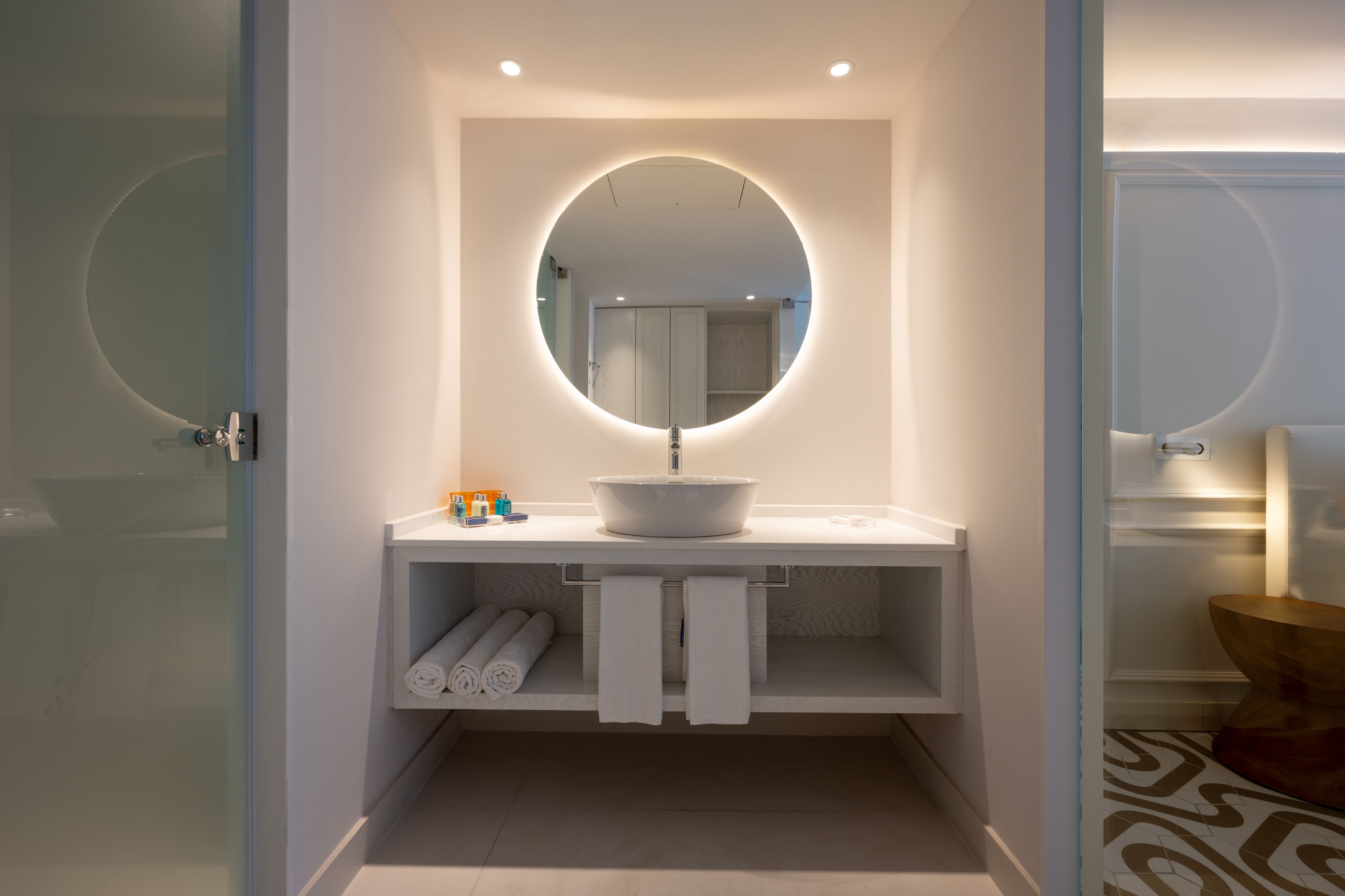 Ein modernes Badezimmer mit rundem Spiegel, weißem Waschtisch und Toilette aus Holz.