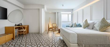 A modern hotel room with a large bed, a desk with a chair, a TV mounted on the wall, and a patterned floor.