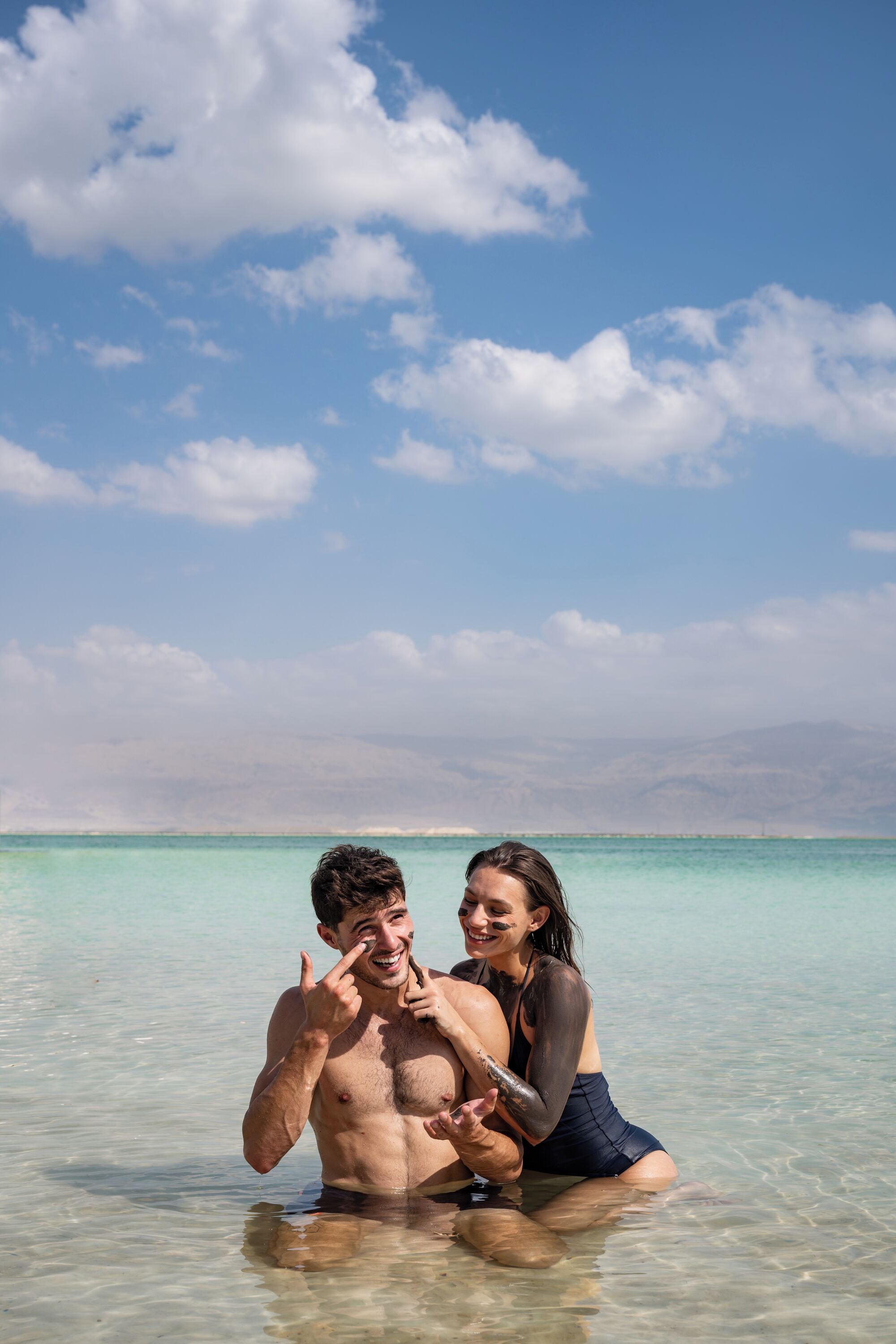 A couple in shallow water with a clear sky and distant mountains.