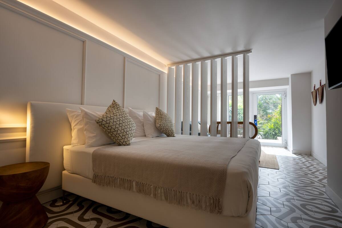 A modern bedroom with a large bed, a wooden side table, and a view of greenery through the window.