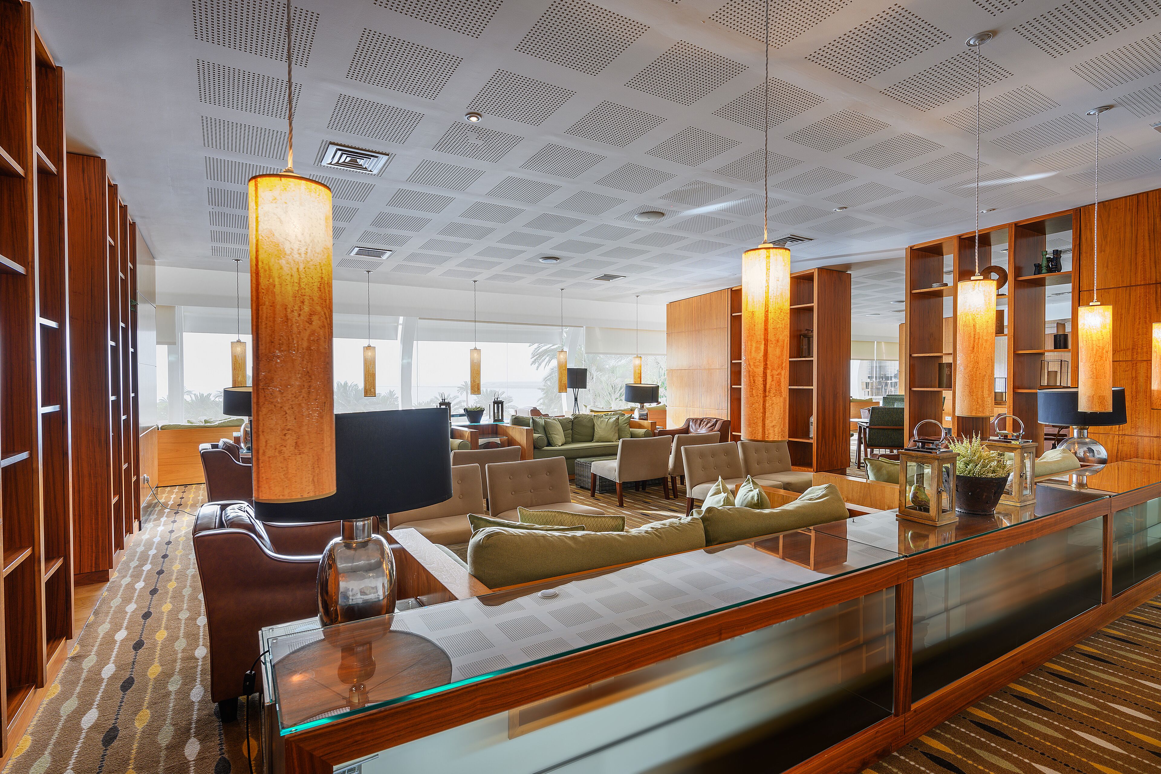 A spacious hotel lobby with a modern design, featuring a large seating area, wooden bookshelves, and a glass partition.