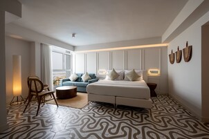 Un dormitorio moderno con una cama grande, un sofá azul, una silla de madera y un suelo estampado.