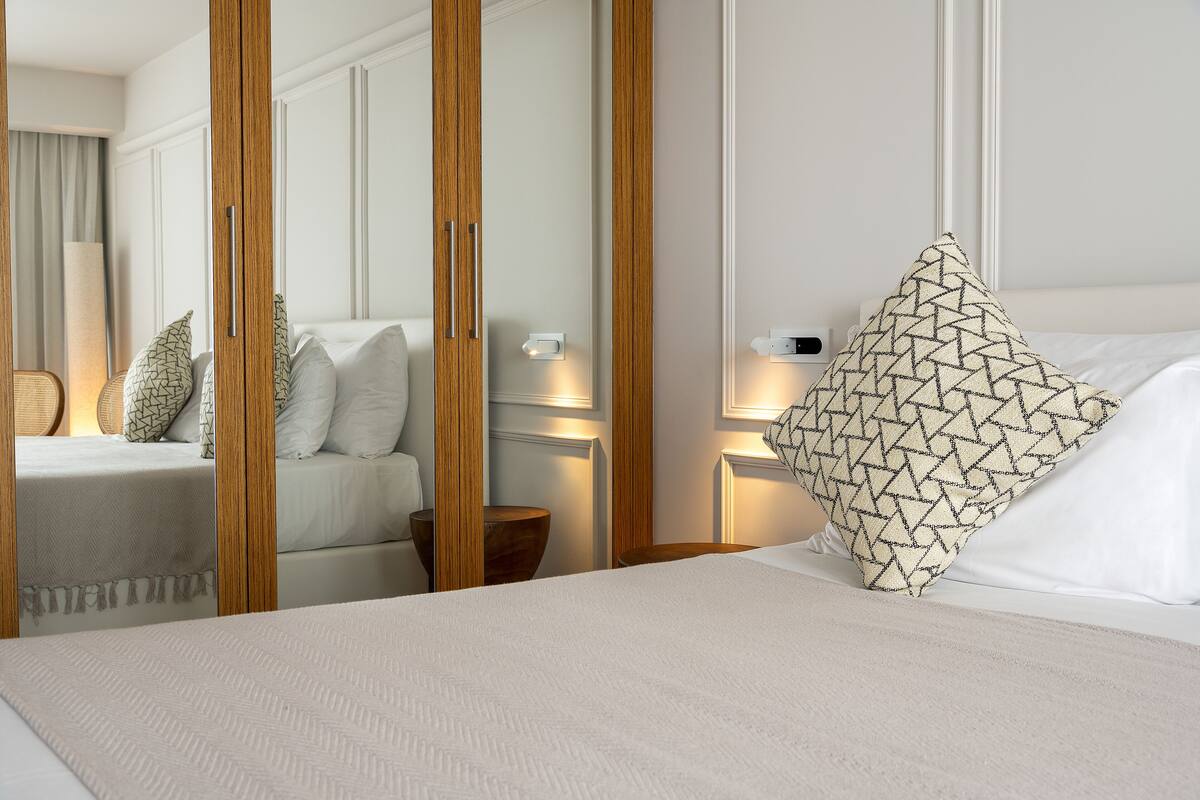 A hotel room with a bed, a wooden wardrobe, a nightstand, and a lamp.