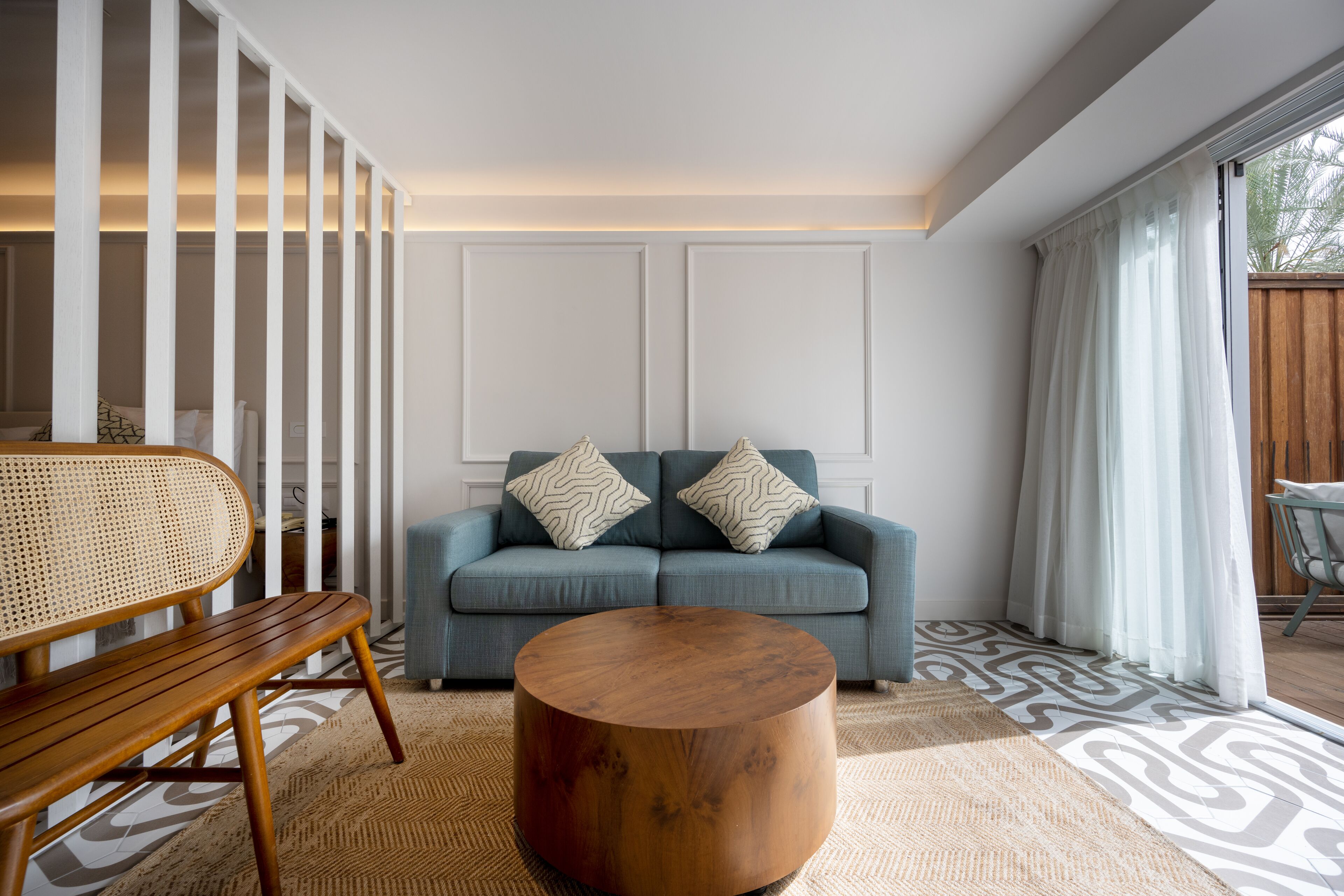 Een moderne woonkamer met een blauwe bank, twee gestreepte kussens, een houten salontafel en een rieten stoel.