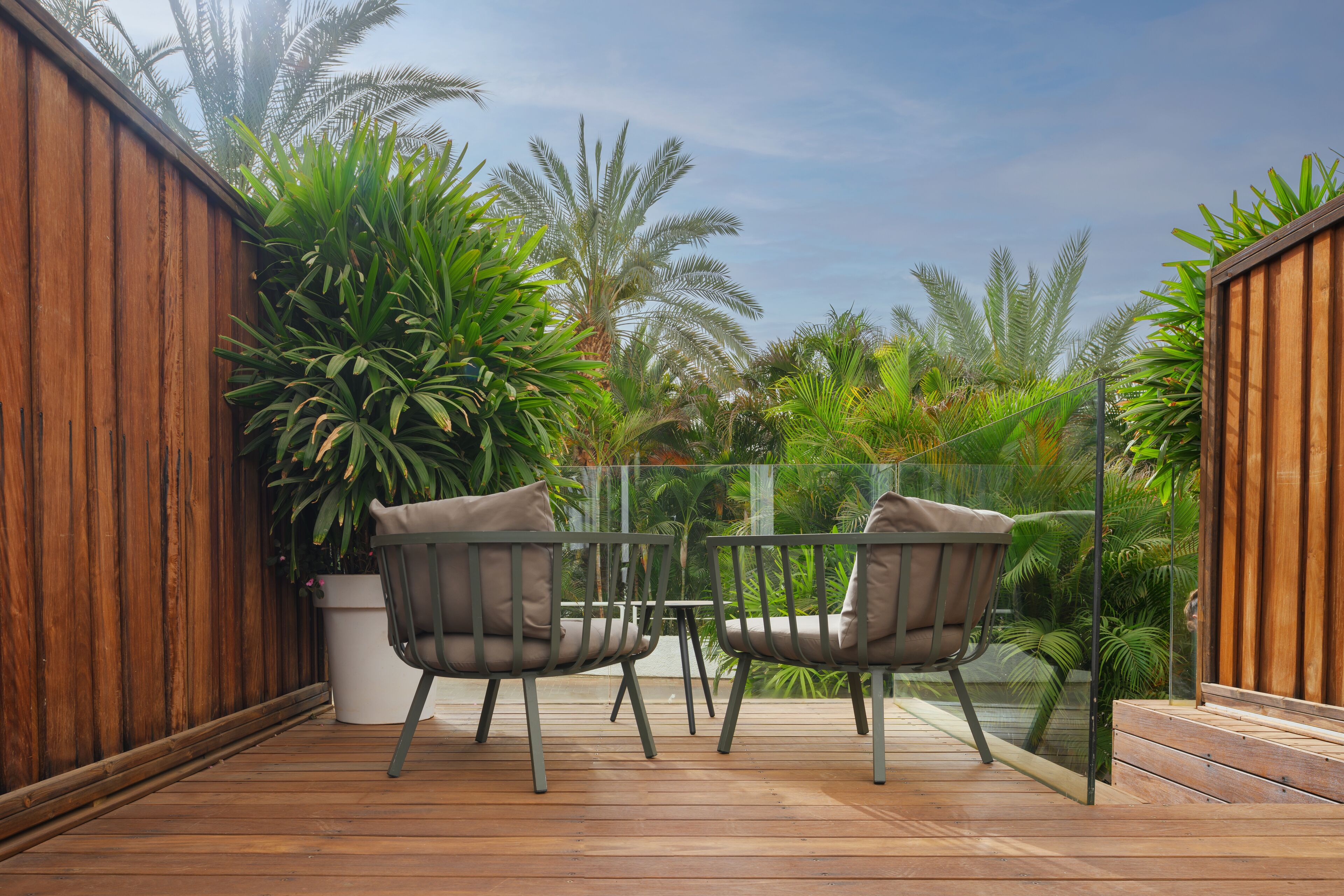 A wooden deck with two chairs and a table, surrounded by lush greenery and palm trees.
