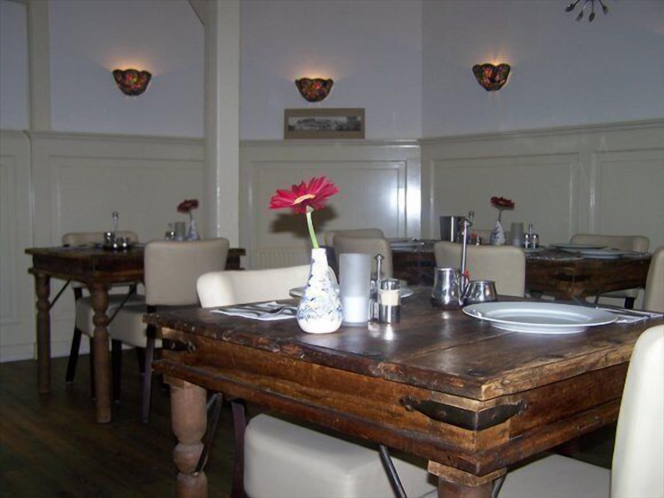 A dining area with wooden tables, white chairs, and a vase with a red flower.