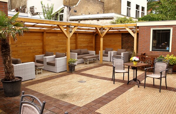 Un área de patio al aire libre con muebles de mimbre, una pérgola y plantas en macetas.