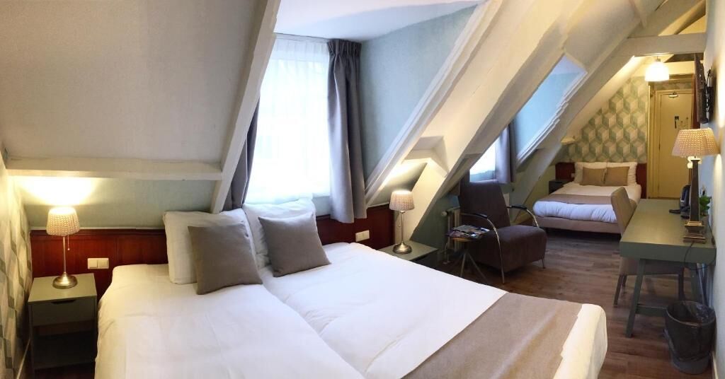 A hotel room with a large bed, a desk, a chair, and a small sofa.