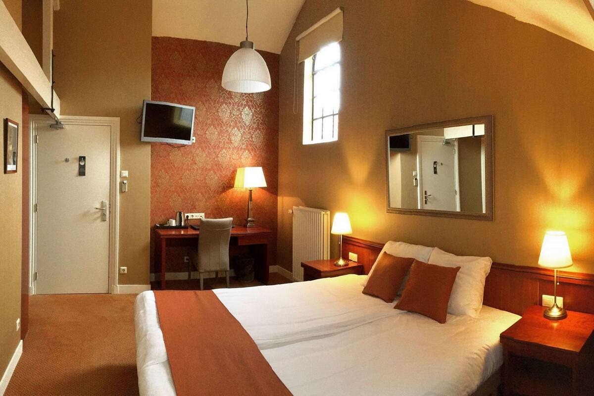 Habitación de hotel con cama, escritorio, silla y televisor montado en la pared.