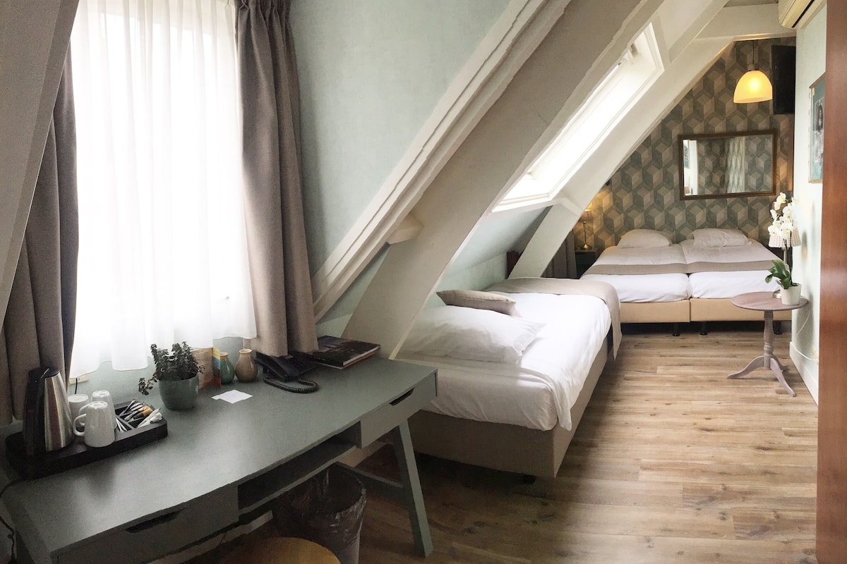 Un dormitorio con escritorio, dos camas, una mesita y una ventana con cortinas.