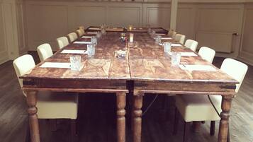 Un salón de conferencias con una larga mesa de madera, sillas blancas y un arreglo floral.