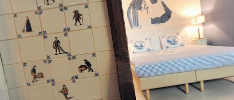 A bedroom with a bed, a nightstand, and a wall with historical tiles.