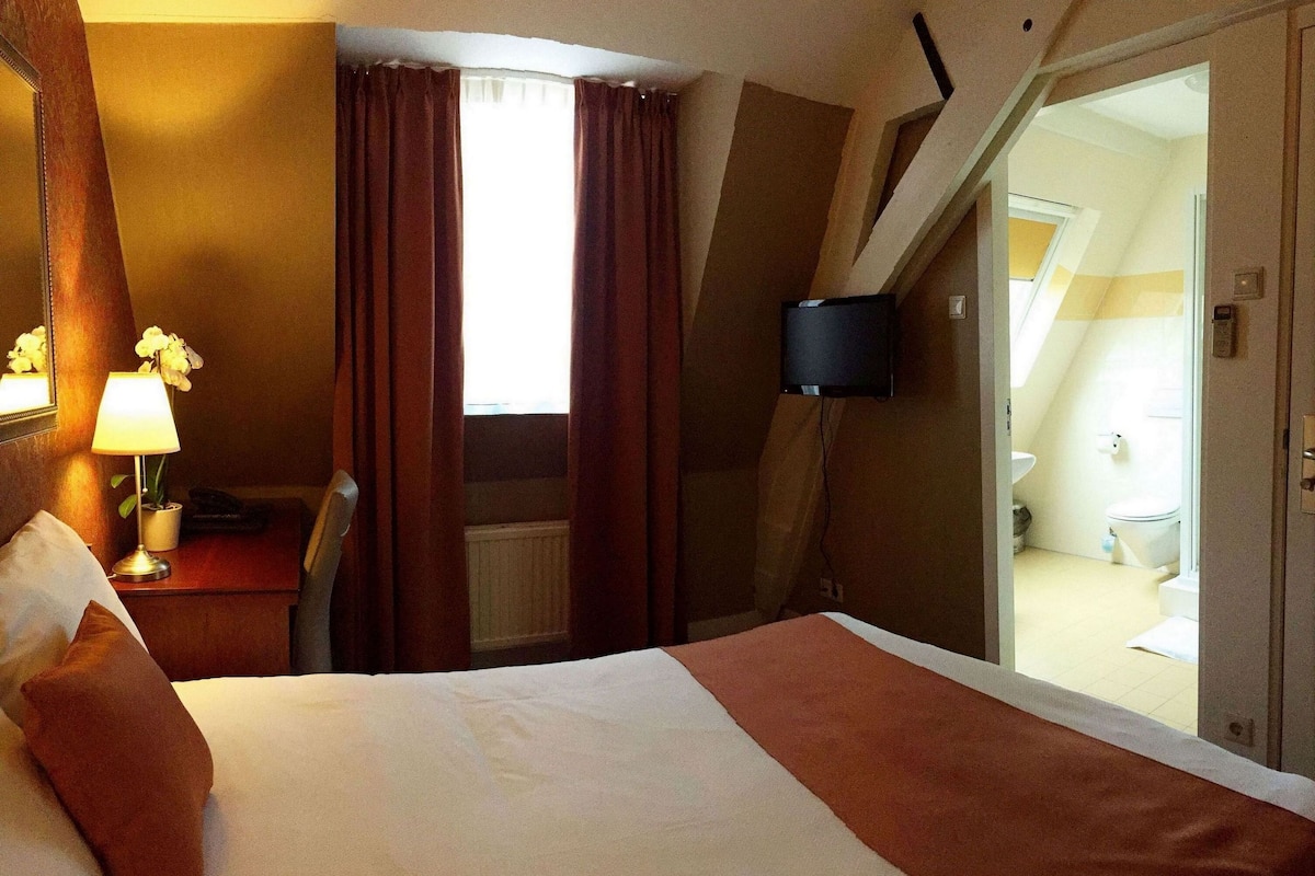 Habitación de hotel con cama, escritorio con lámpara, silla y vista al baño.