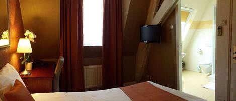 A hotel room with a bed, a desk with a lamp, a chair, and a view of the bathroom.