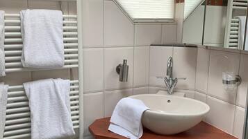 A bathroom with a white sink, a towel rack with towels, a mirror, and a window with blinds.