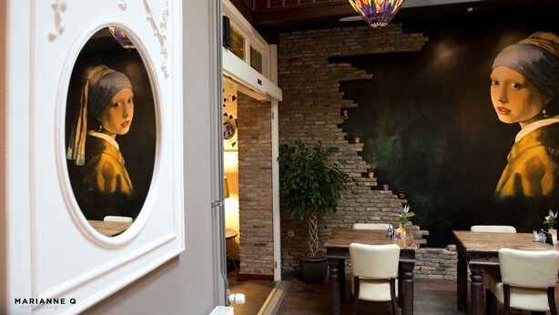 A dining area with a large mirror reflecting a painting, a staircase, and a hanging light fixture.