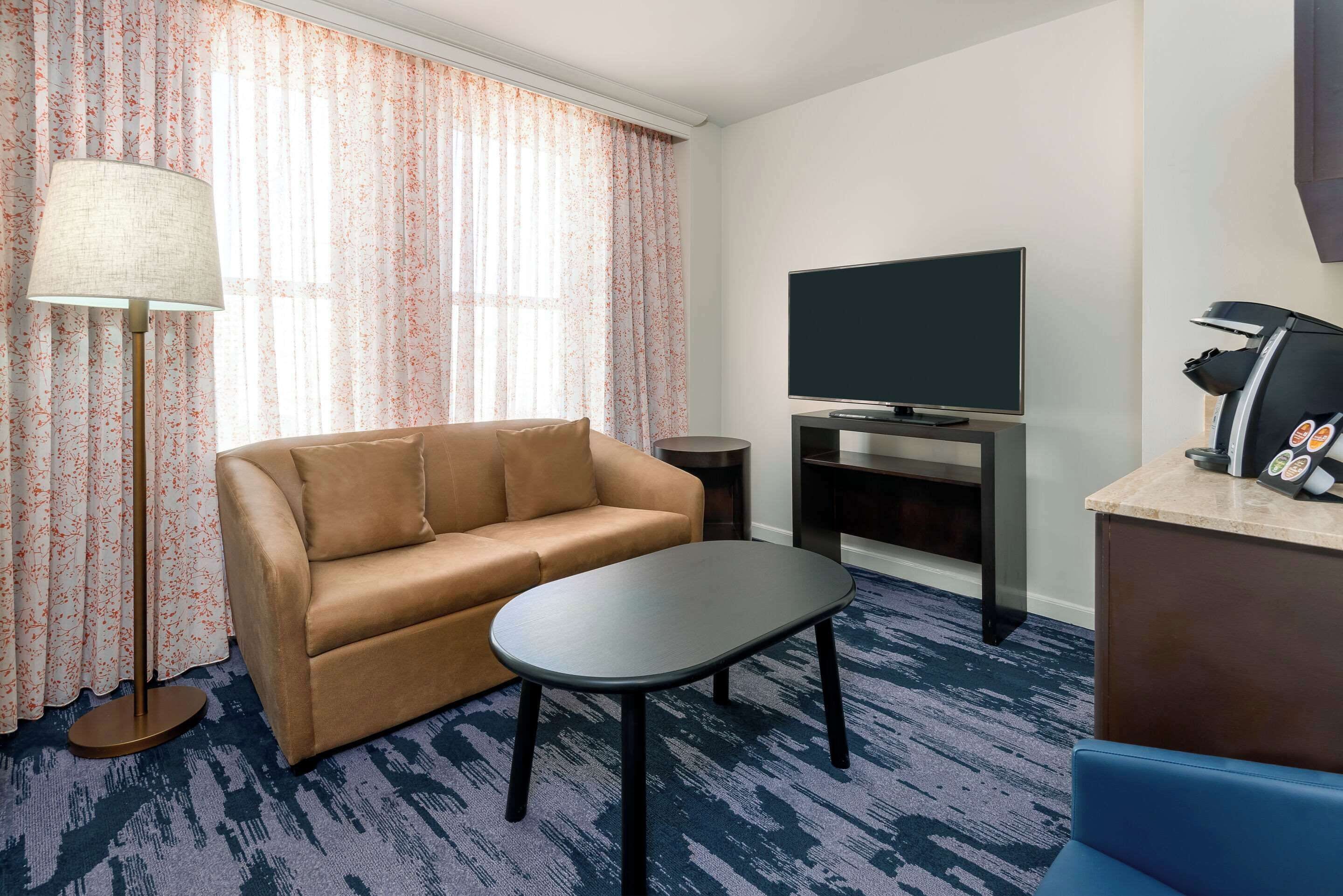 A hotel room with a sofa, a small table, a TV, a massage chair, and a lamp.