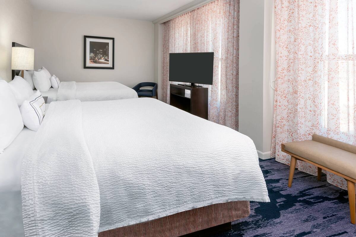 A hotel room with a large bed, a TV, a desk, and a bench.