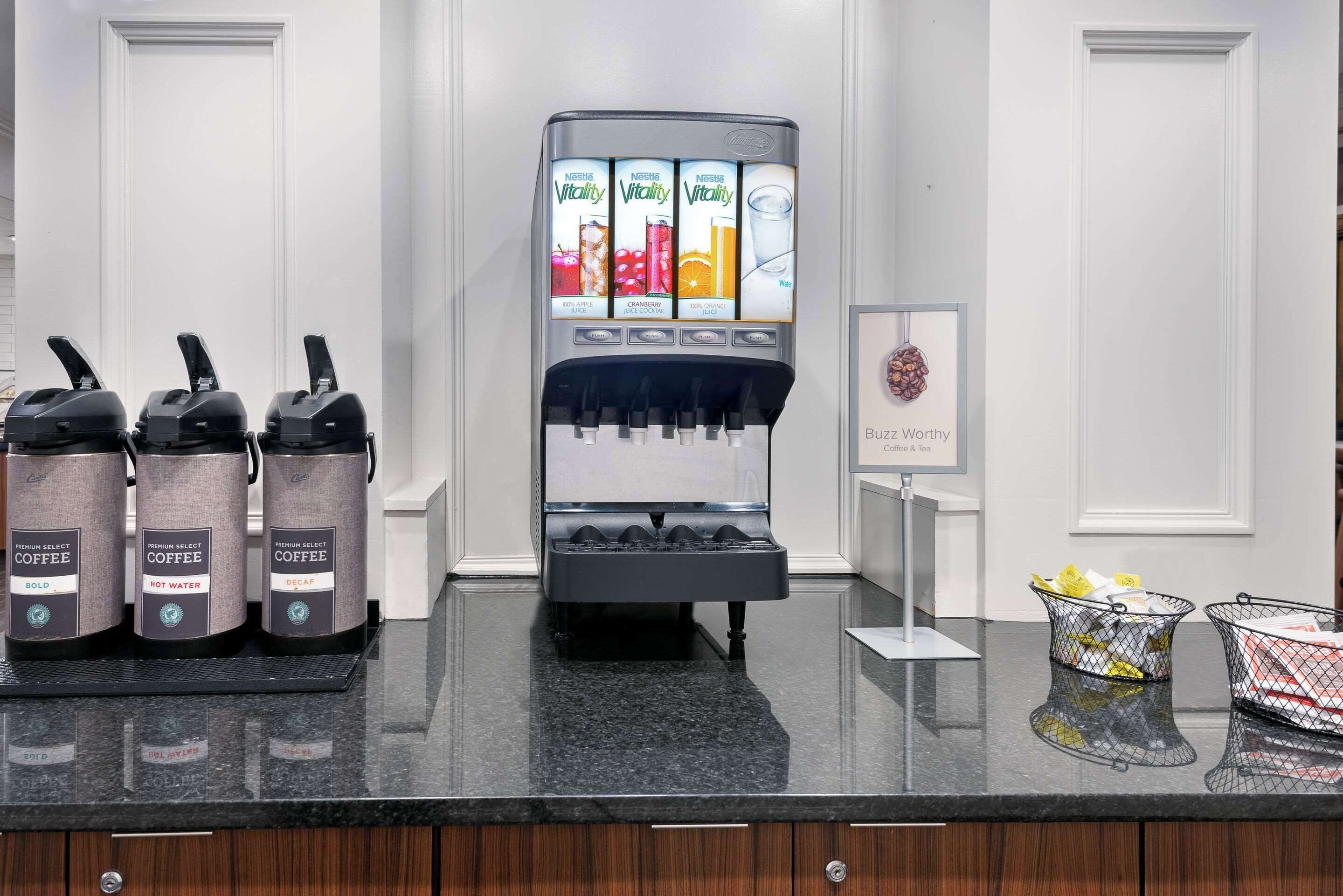 A coffee station with a coffee machine and three coffee dispensers labeled "Premium Select Coffee," "Bold," "Hot Water," and "Decaf."