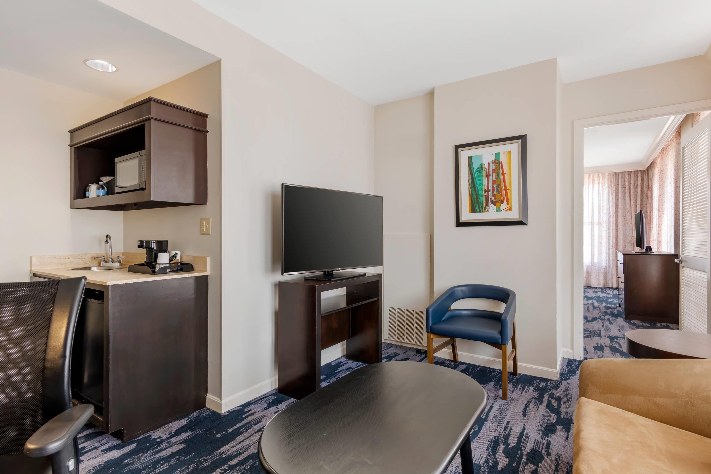 Une chambre d’hôtel équipée d’une kitchenette, d’un téléviseur à écran plat, d’un canapé, d’un fauteuil et d’un tableau au mur.