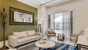 A modern living room with a beige sofa, a round coffee table, and a large mirror. There is a floor lamp and a chair near the window. - The Connally Hotel Downtown Atlanta, an Ascend Collection Hotel (Atlanta)