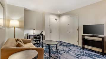 A hotel room with a sofa, a small round table, a TV on a stand, a desk with a chair, and a shower area.