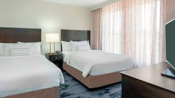 A hotel room with two beds, a desk, a lamp, and a TV.
