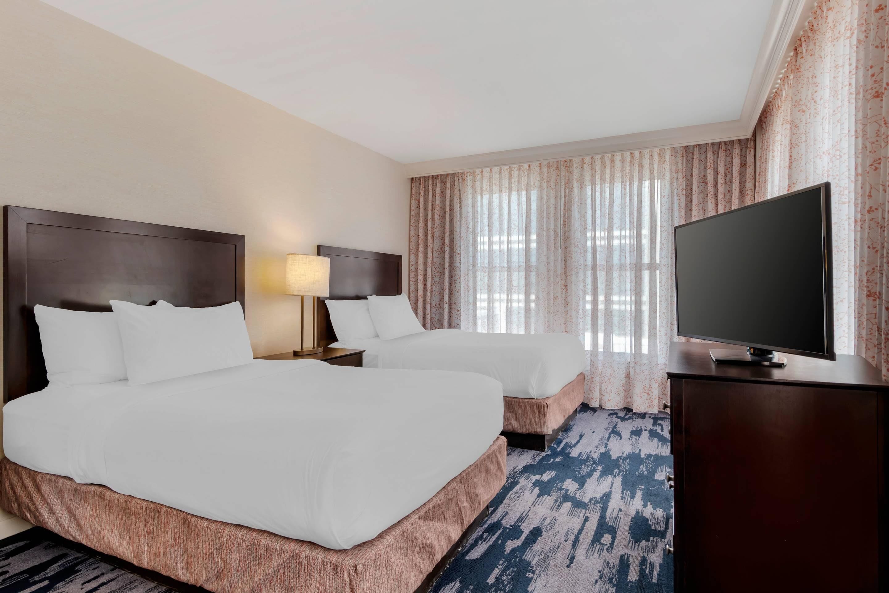 A hotel room with two beds, a television, and a window with curtains.