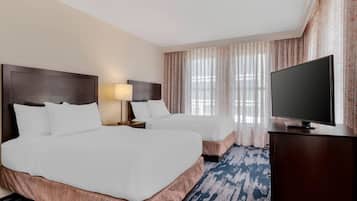 A hotel room with two beds, a television, and a window with curtains.
