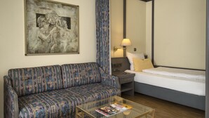 Une chambre d’hôtel avec un canapé, un lit, une table basse en verre sur laquelle se trouve un magazine, une lampe et un tableau au mur.