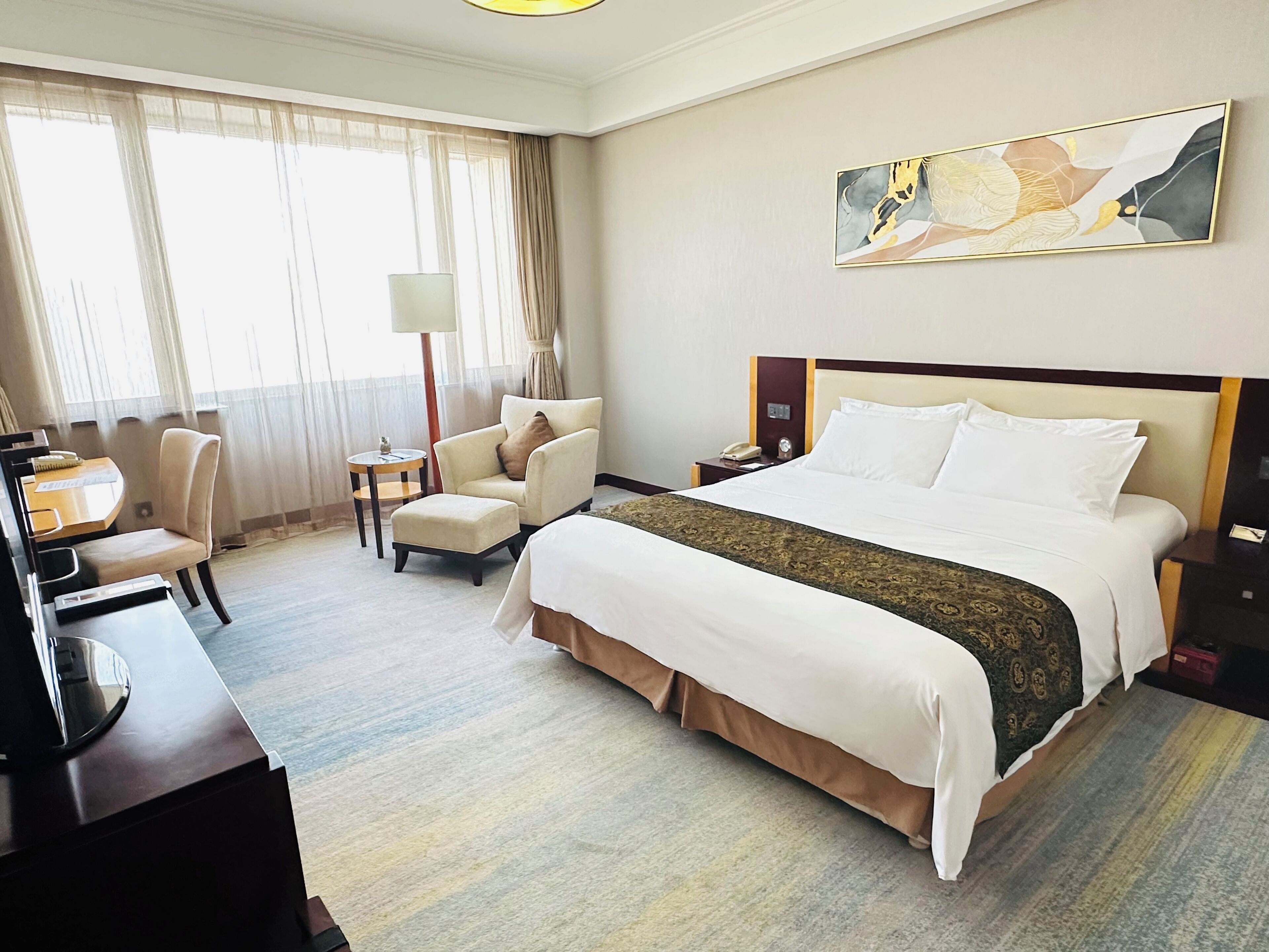 A hotel room with a large bed, a desk, a chair, and a small table.