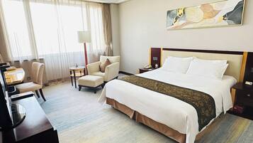 A hotel room with a large bed, a desk, a chair, and a small table.