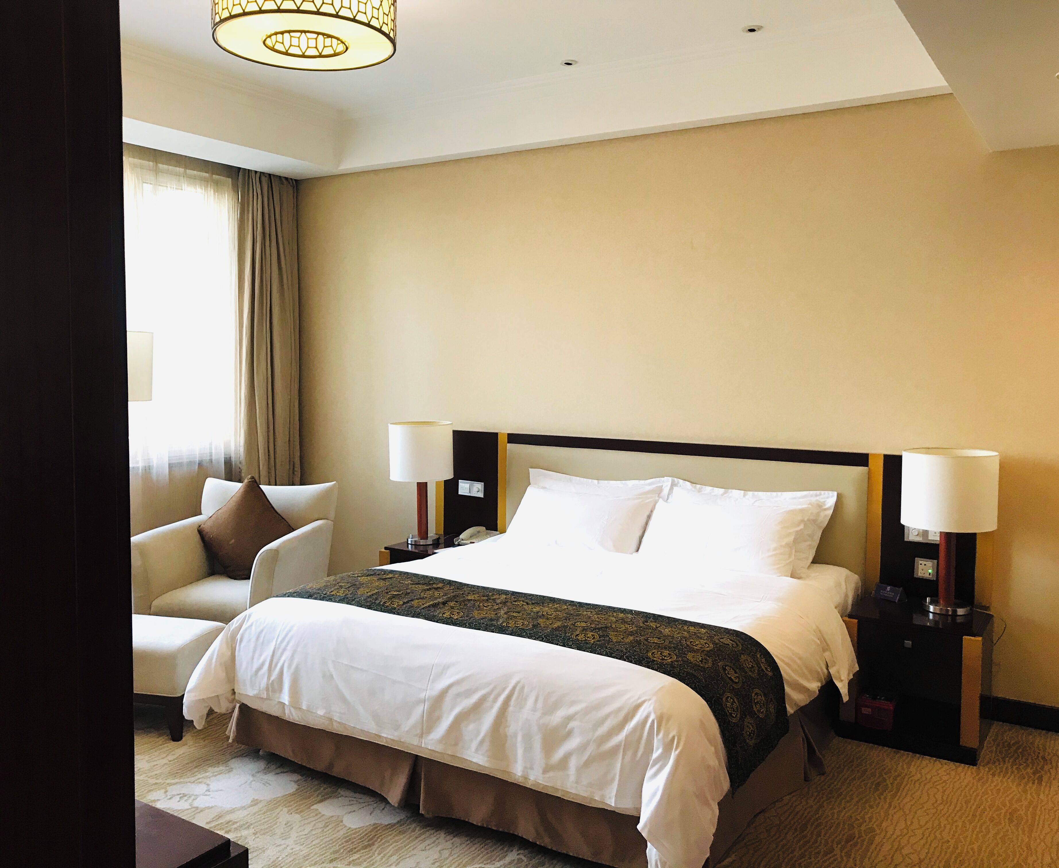 Quarto de hotel com cama, duas mesas de cabeceira, uma cadeira e um abajur.
